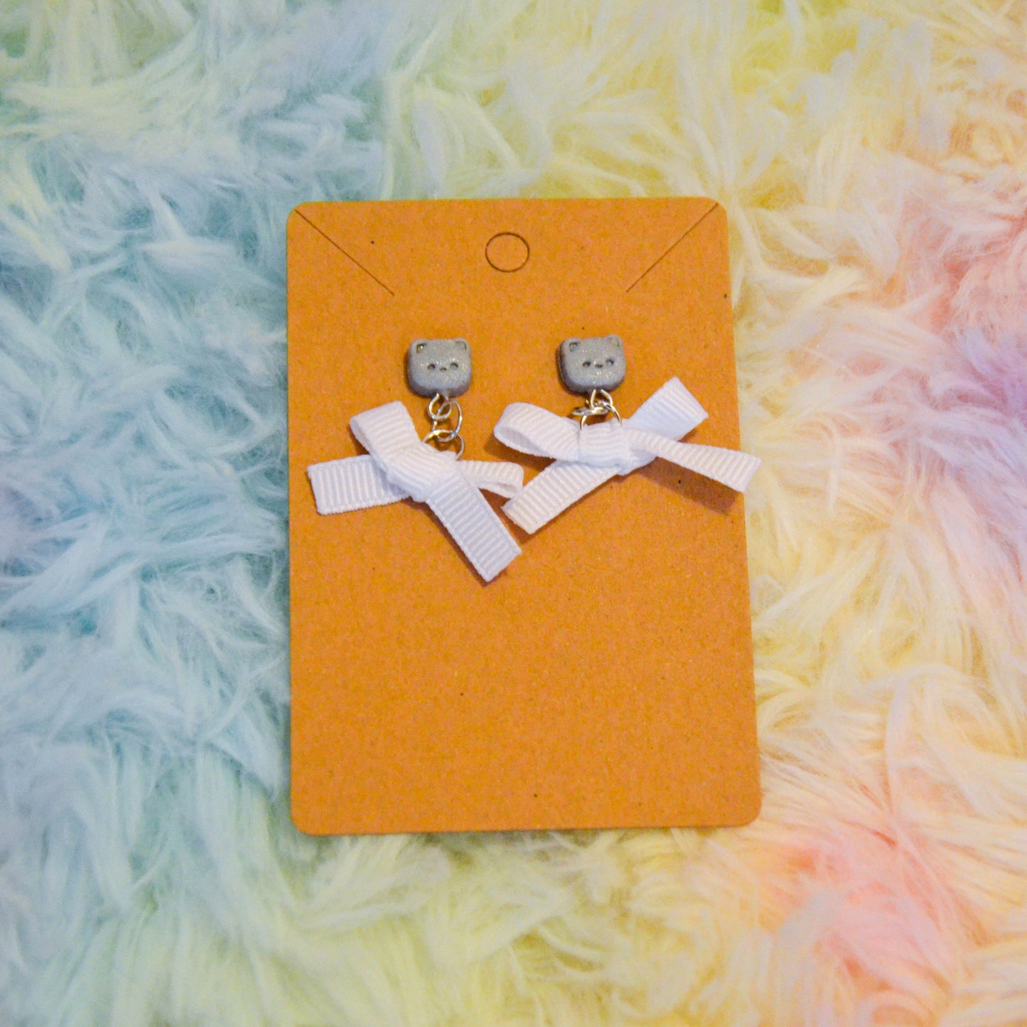 Silver pomeranian bow earrings against rainbow background