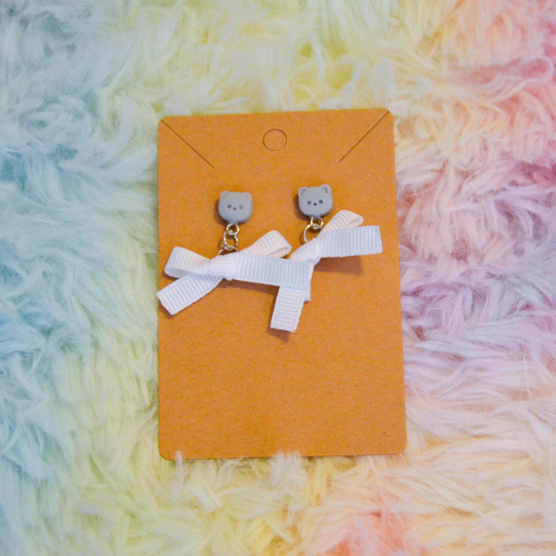 Gray pomeranian bow earrings against rainbow background