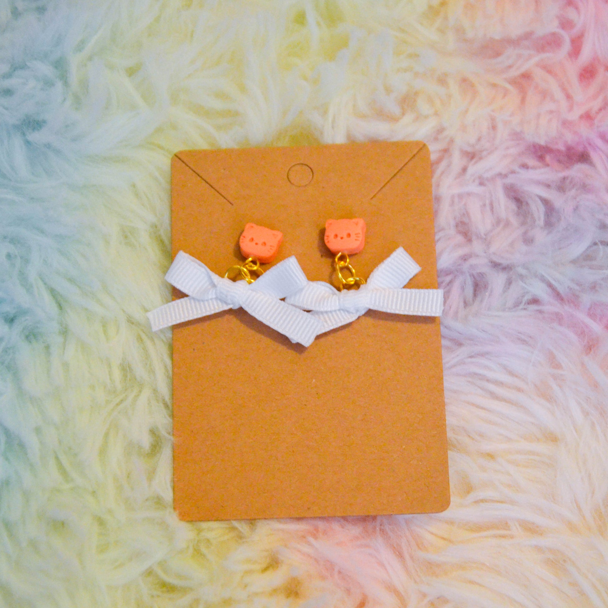 Orange cat bow earrings against rainbow background