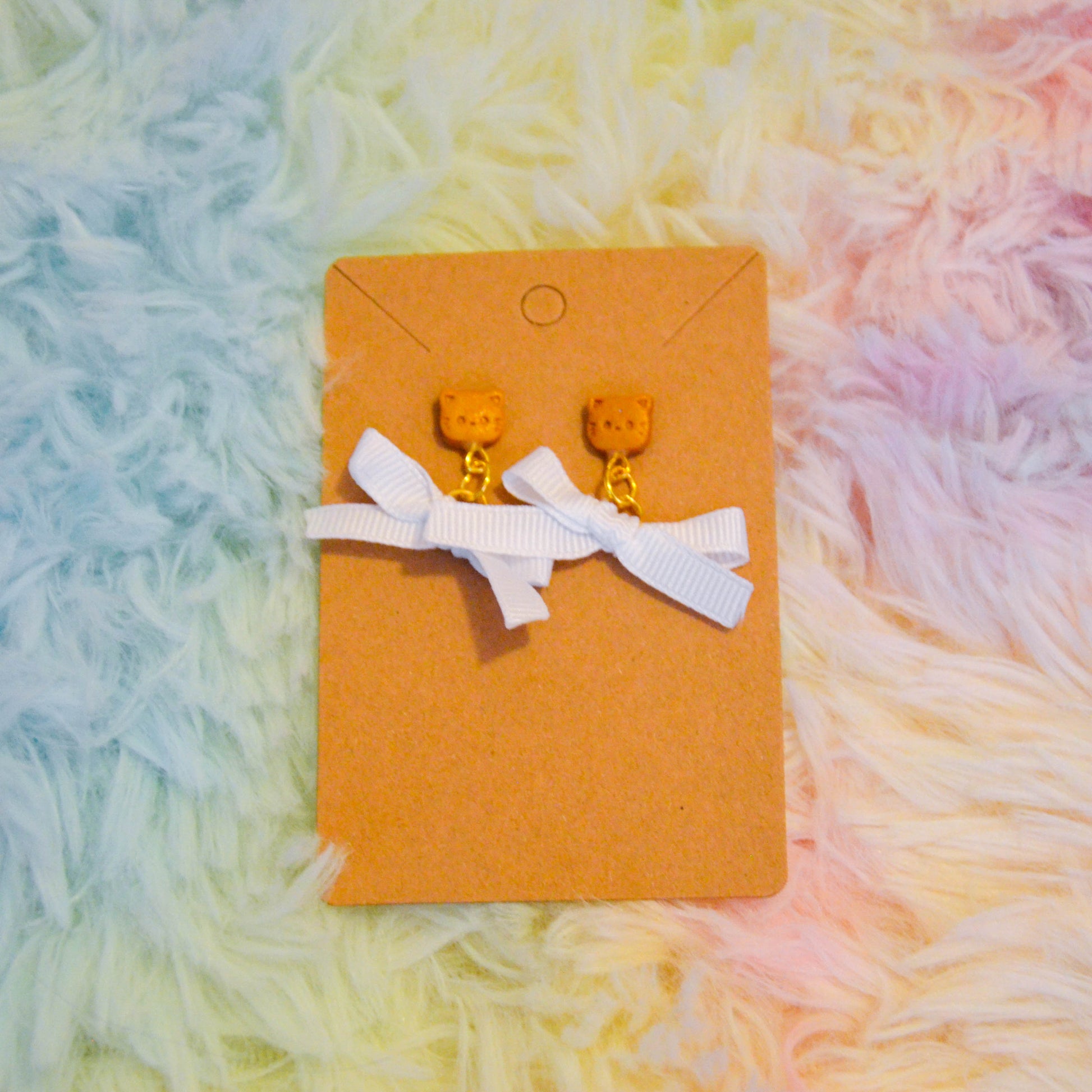 Gold cat bow earrings against rainbow background