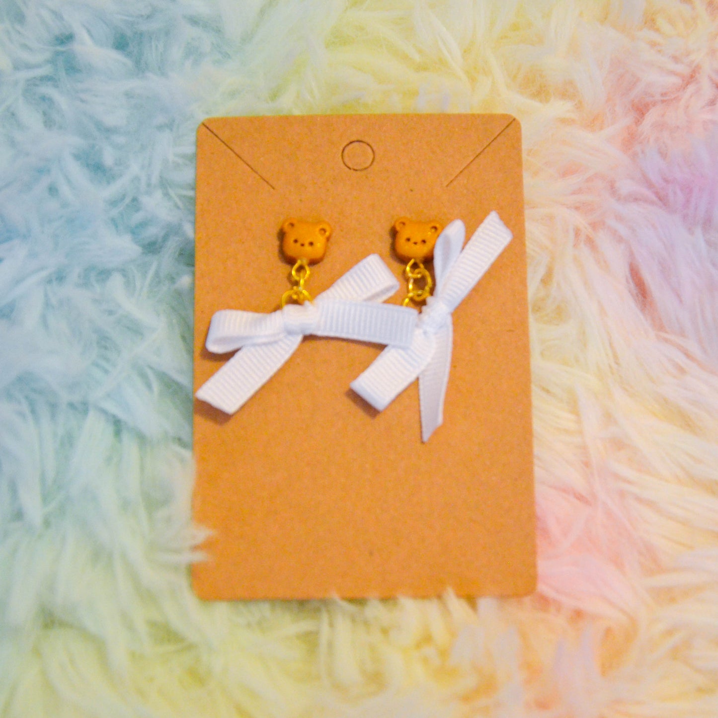 Gold bear bow earrings against rainbow background