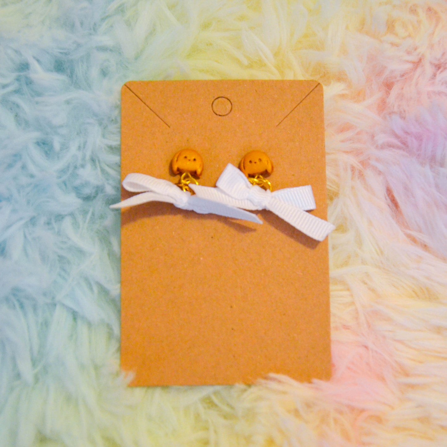 Gold bunny bow earrings against rainbow background