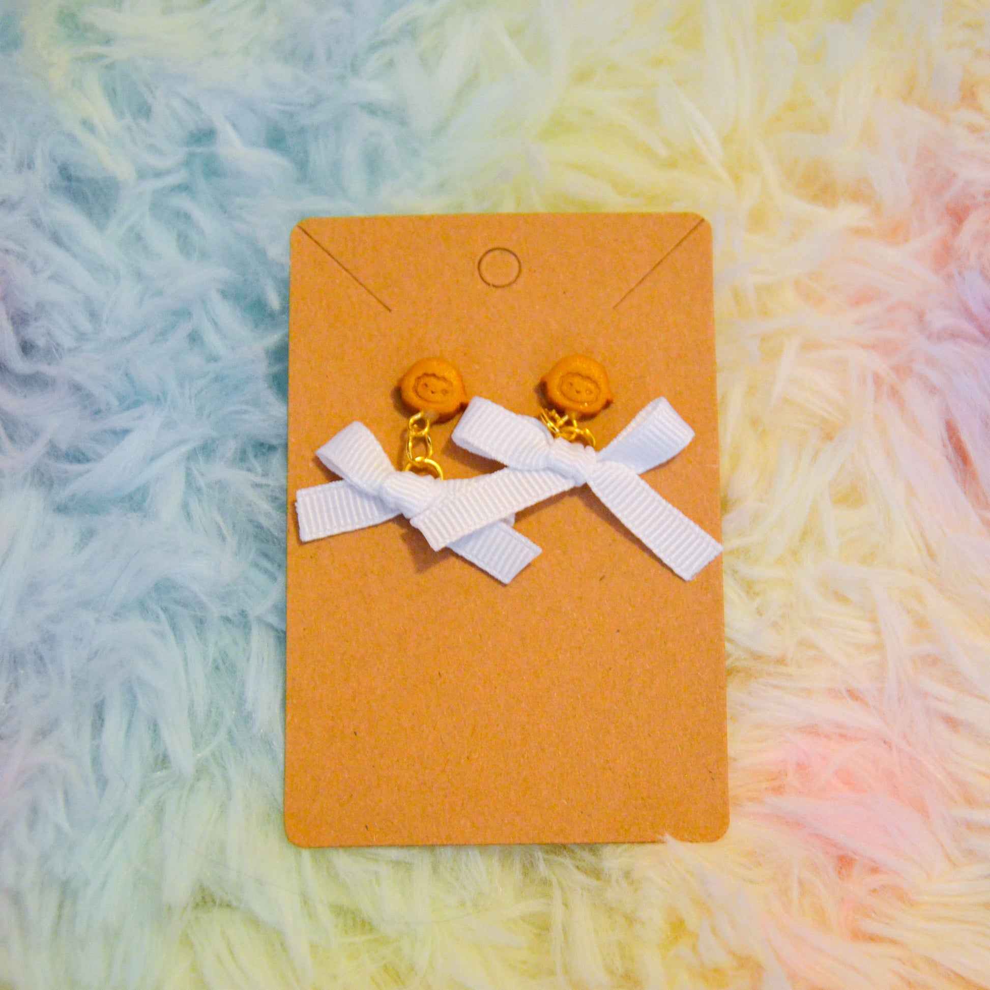 Gold sheep bow earrings against rainbow background