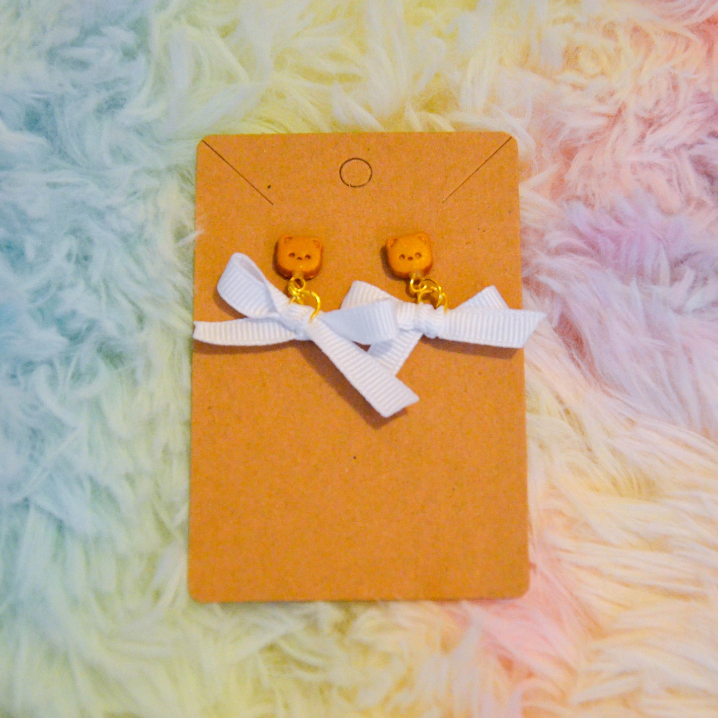 Gold pomeranian bow earrings against rainbow background