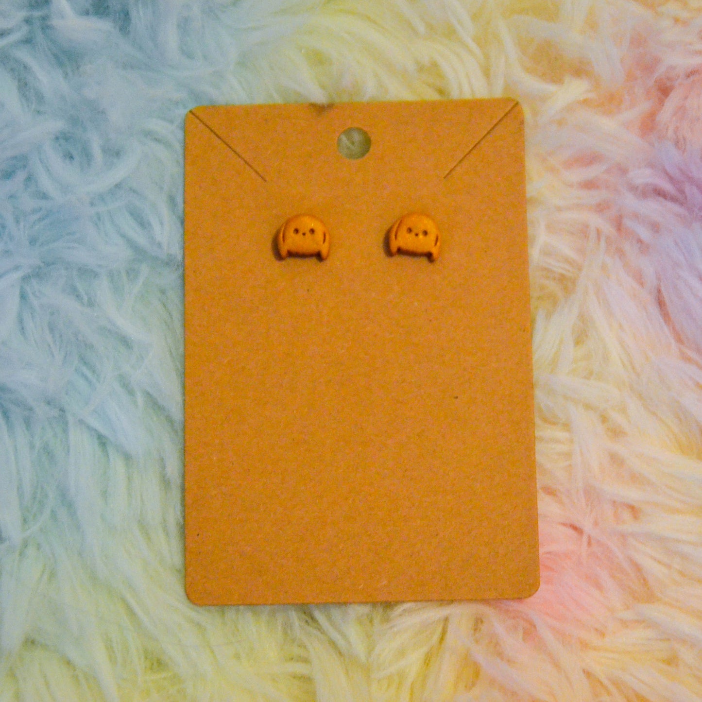 Gold bunny stud earrings against rainbow background