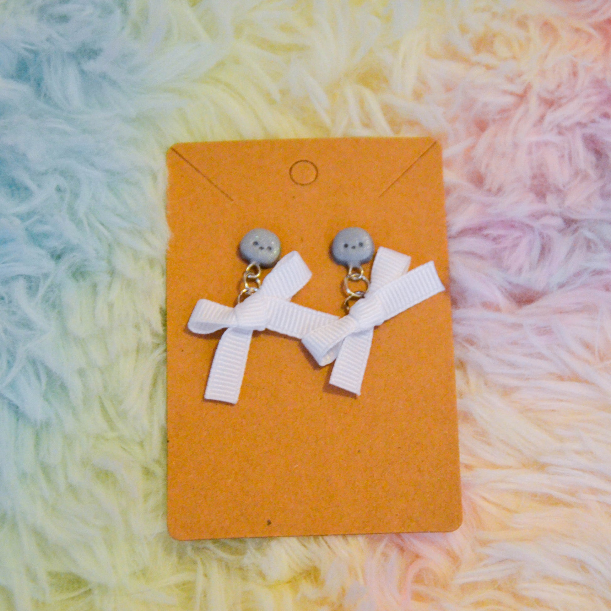 Silver chick bow earrings against rainbow background