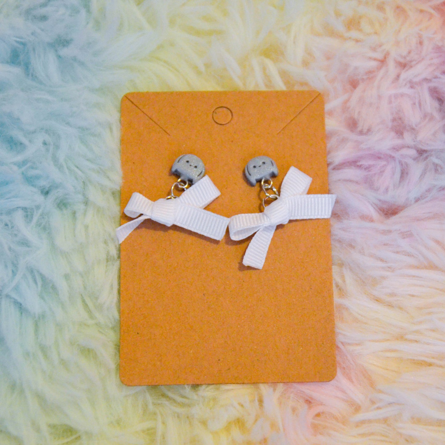 Silver bunny bow earrings against rainbow background