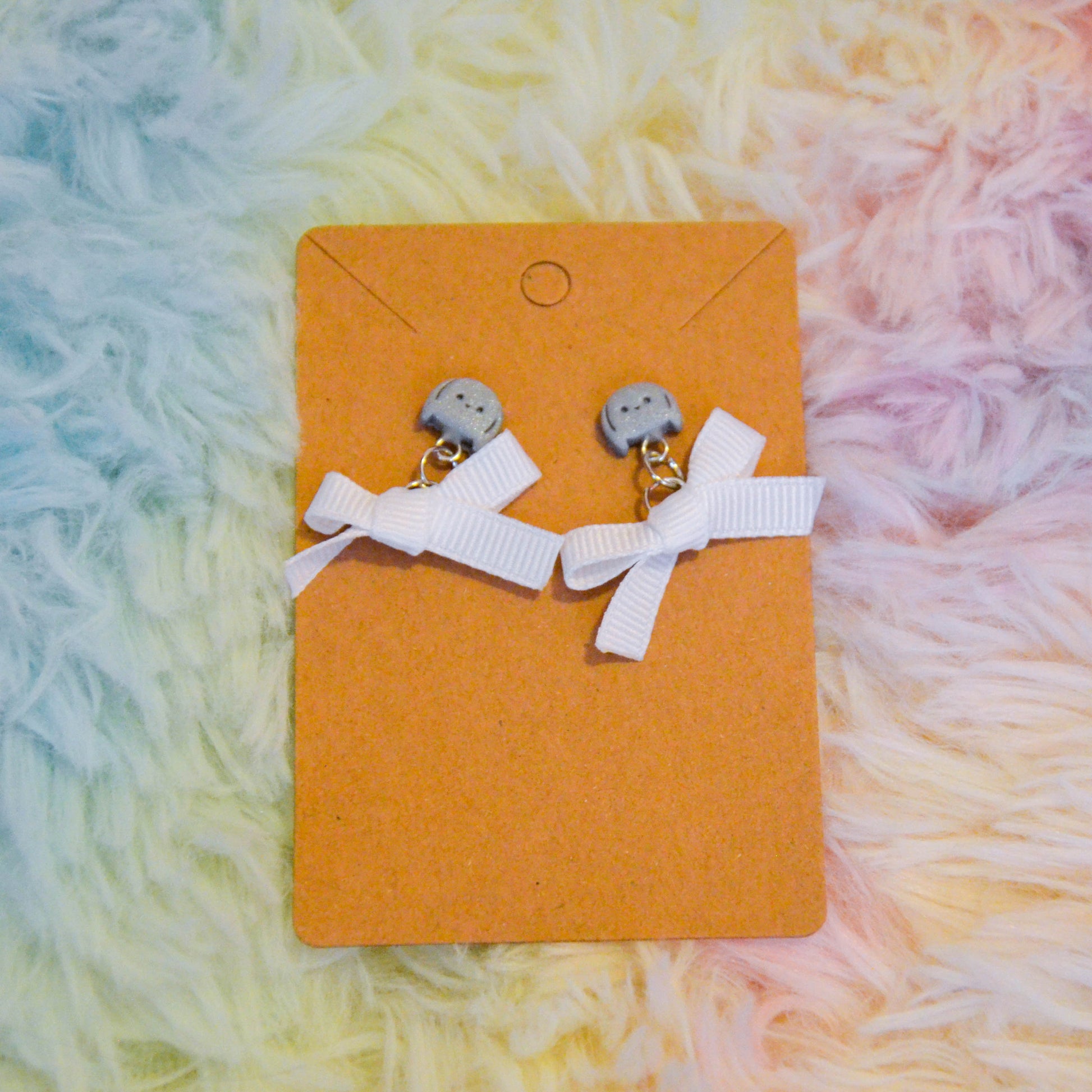 Silver bunny bow earrings against rainbow background