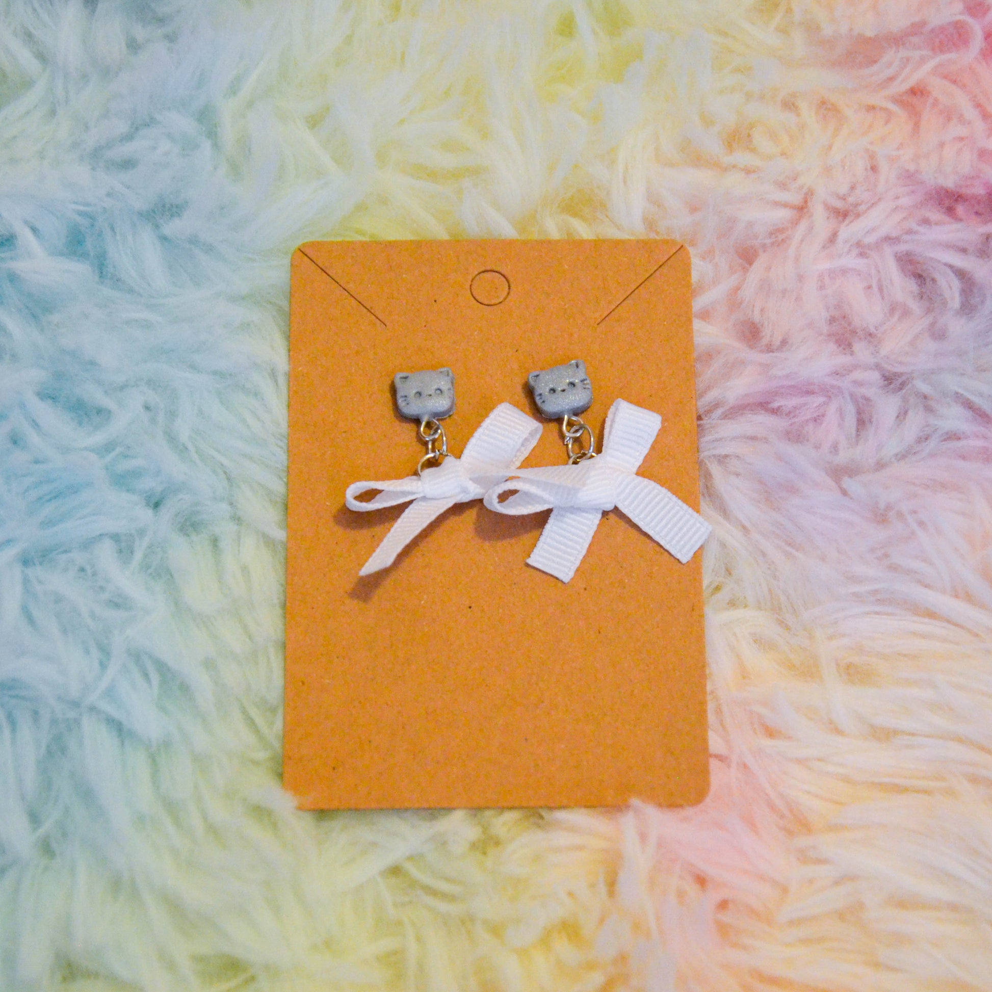 Silver cat bow earrings against rainbow background