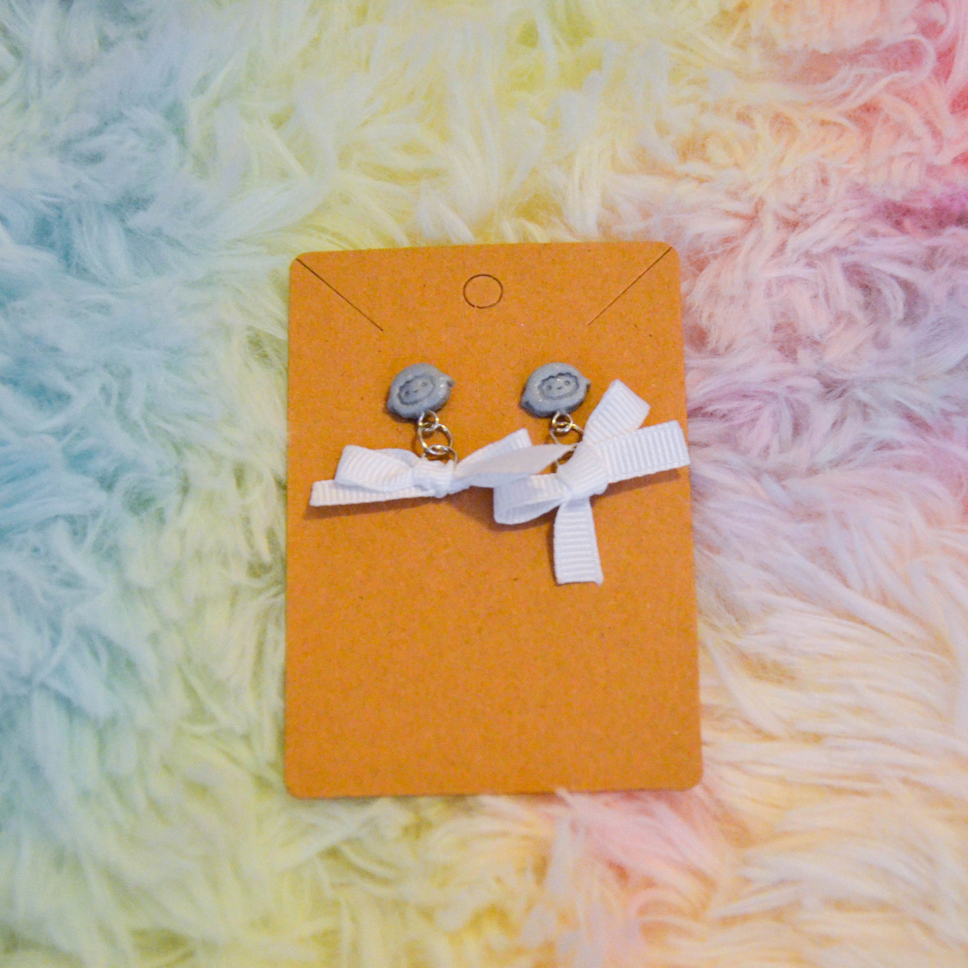 Silver sheep bow earrings against rainbow background