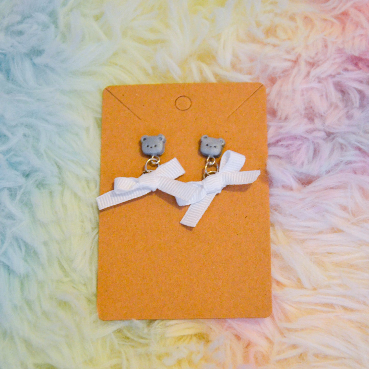 Silver bear bow earrings against rainbow background